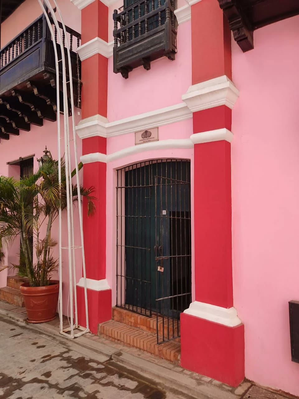 Entrada de la Casa Rosada: puerta con reja negra entre dos columnas rojas y la placa de la Universidad Simón Bolívar encima